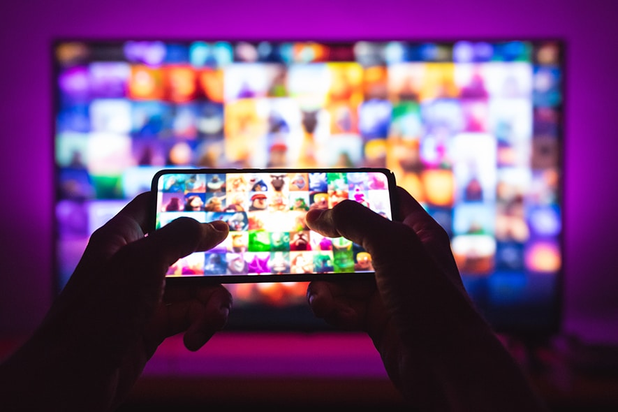 Hands holding a remote control in front of a TV screen.